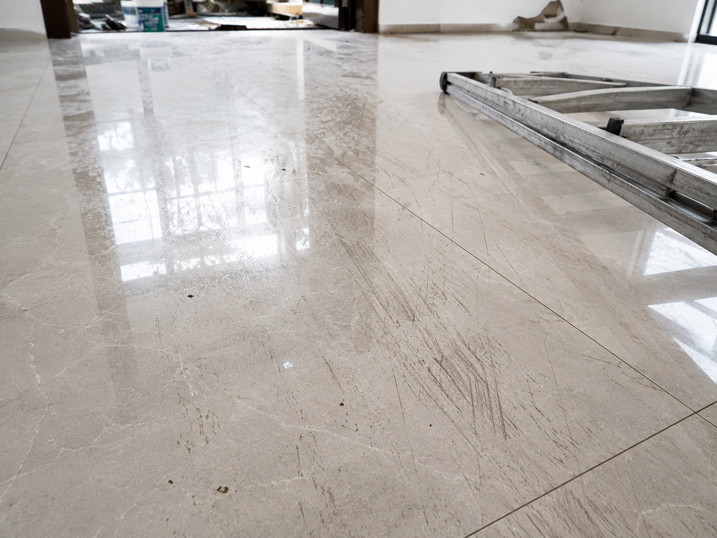 Cận cảnh nền gạch porcelain xuất hiện các vết trầy xước do kéo lê thang nhôm và dụng cụ thi công, công trình đang hoàn thiện, ảnh chụp thực tế, độ chi tiết cao, không watermark.